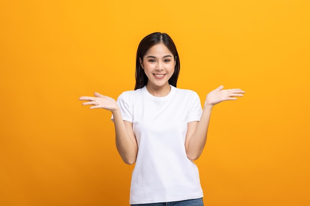 Excited Surprised asian woman with hands on isolated background. Happy shocked face female wow promotion advertising concept. Joyful teenage girl in white shirt standing in yellow room.