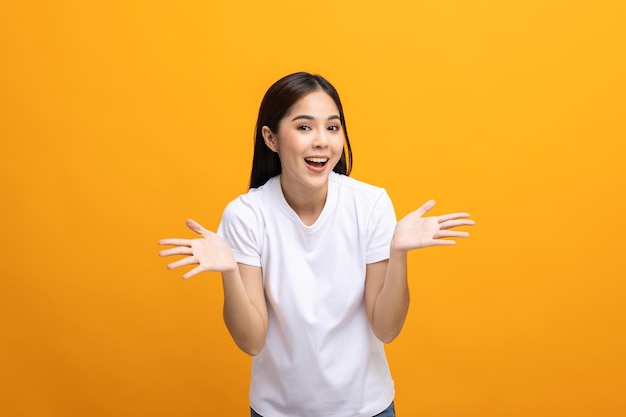 Excited Surprised asian woman with hands on isolated background. Happy shocked face female wow promotion advertising concept. Joyful teenage girl in white shirt standing in yellow room.