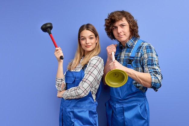 Excited team of two plumbers dressed in blue uniform with plunger, being glad to repair bathtub