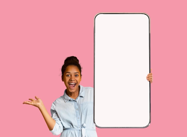 Excited teen black girl showing smartphone with empty screen