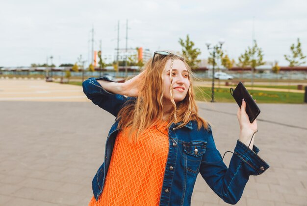 An excited teenage girl is dancing and listening to music with headphones and a smartphone on the street generation z