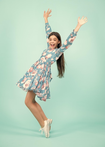 Excited teenager amazed and cheerful emotions Happiness freedom motion and child Young teenager girl wear summer dress jumping in air over blue background