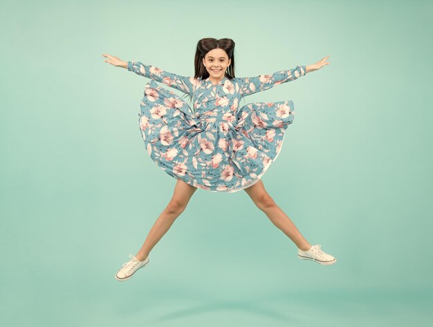 Excited teenager amazed and cheerful emotions Teenager girl jumping Full length of her she playful preteen teenager girl having fun and jumping in fun star pose isolated on blue background