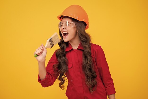Excited teenager builder expert in helmet on construction site teen girl painter with painting brush tool or paint roller child on repairing work renovation concept