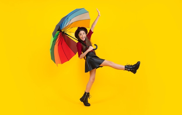 Excited teenager glad amazed and overjoyed emotions Teen girl under rainbow umbrella in autumn weather isolated on yellow background Autumn kids clothes