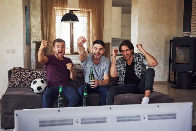 Excited three friends watching soccer on TV at home together.