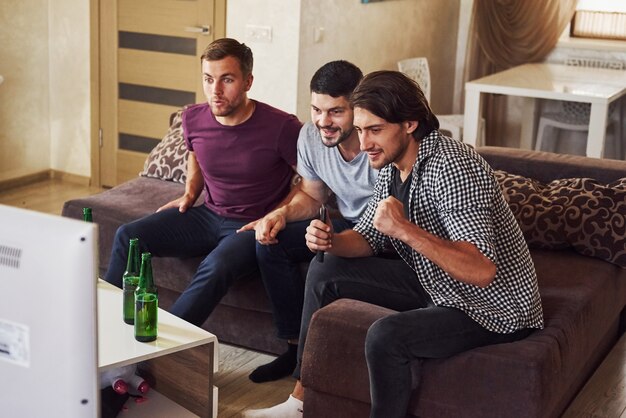 Tre amici eccitati che guardano insieme il calcio in tv a casa.