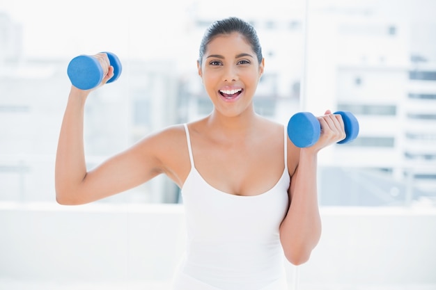 Excited toned brunette holding dumbbells