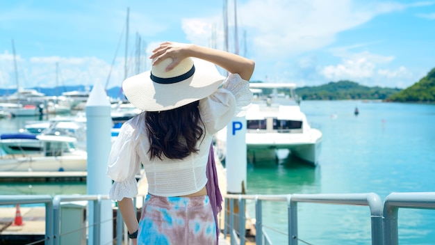 An excited tourist in white hat enjoying and standing on the dock with luxury yachts during summer