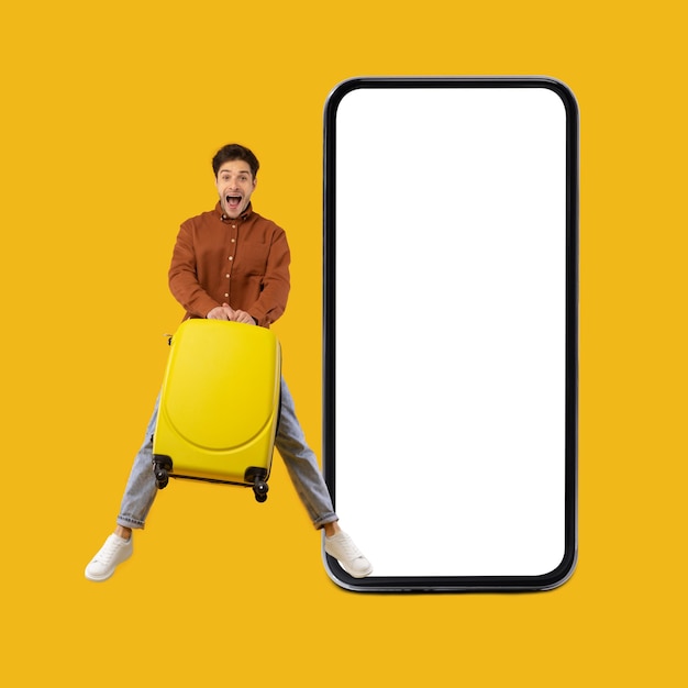 Excited traveler guy jumping near large cellphone on yellow background