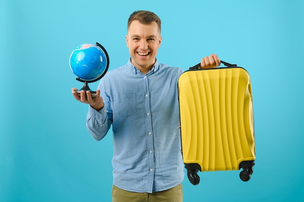 Excited traveler tourist man isolated on blue background. Passenger traveling abroad on weekends. Air flight journey concept. Holding world globe.