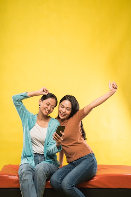 Excited two beautiful asian girl with hands up while looking smartphone