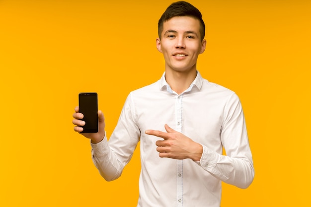 Excited winner Asian man pointing at mobile phone after received good news isolated on yellow background in studio. - image