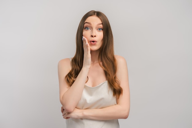 Excited woman in dress feeling shocked and surprised holding hand on face