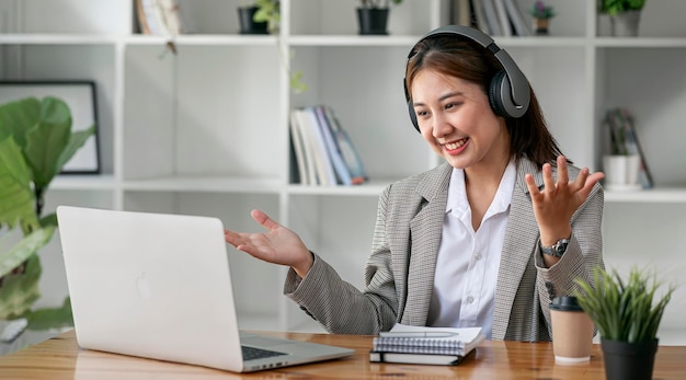 Excited woman in headphones having conversation on video chat online while using laptop at home.