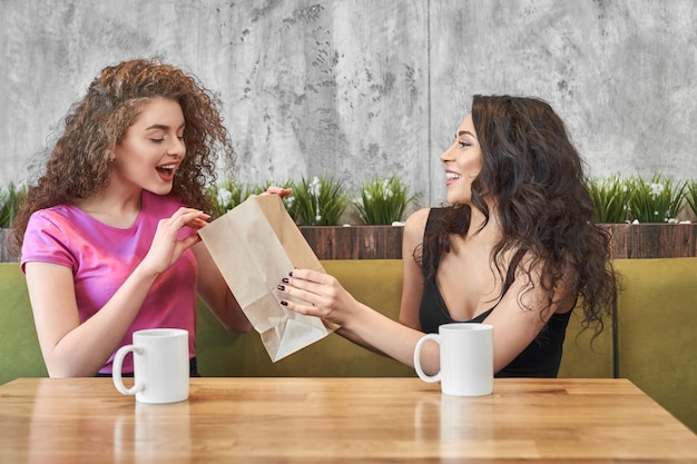 Excited woman looking at package and taking gift in cafe