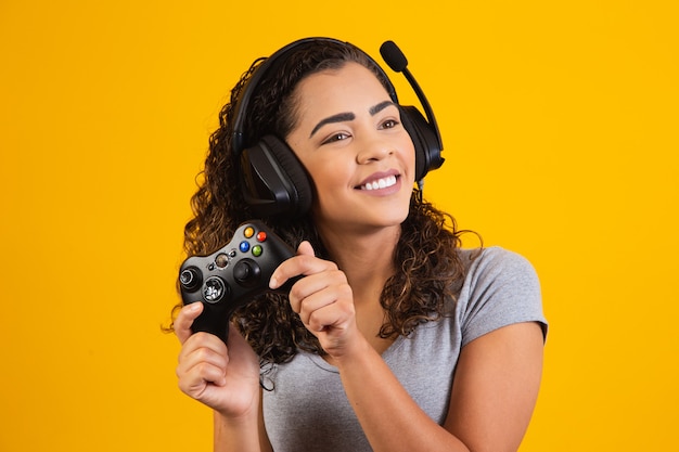 Excited woman playing video game on yellow background.