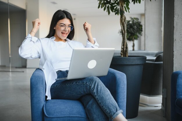 Excited woman reading good news on laptop sitting in a coffee shop terrace