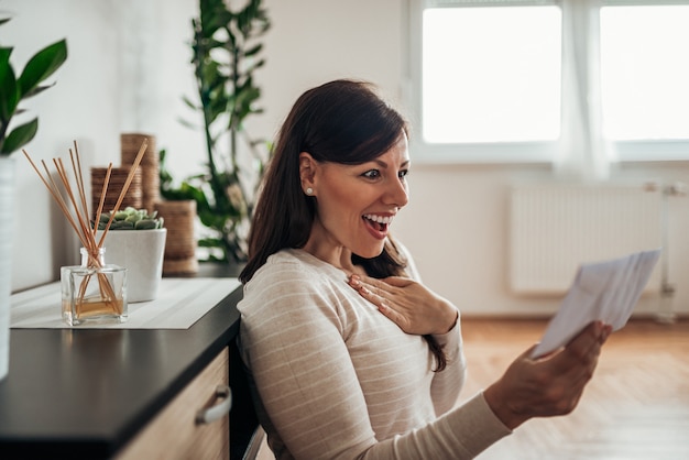 Excited woman reading a letter with good news at home.