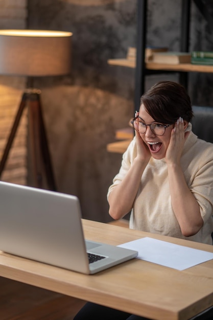 Una donna eccitata seduta al laptop e in attesa degli aggiornamenti