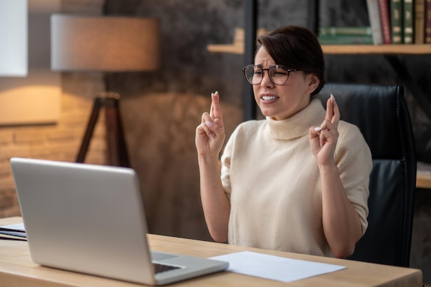 Una donna eccitata seduta al laptop con le dita incrociate