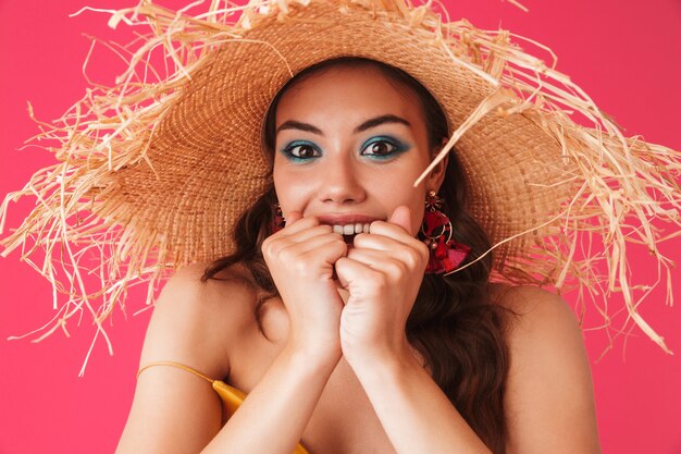 Excited woman wearing big straw hat biting fists in delight