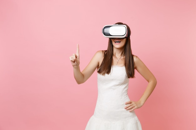 Donna eccitata in abito bianco, auricolare della realtà virtuale tocca qualcosa come premere il pulsante o puntare allo schermo virtuale mobile