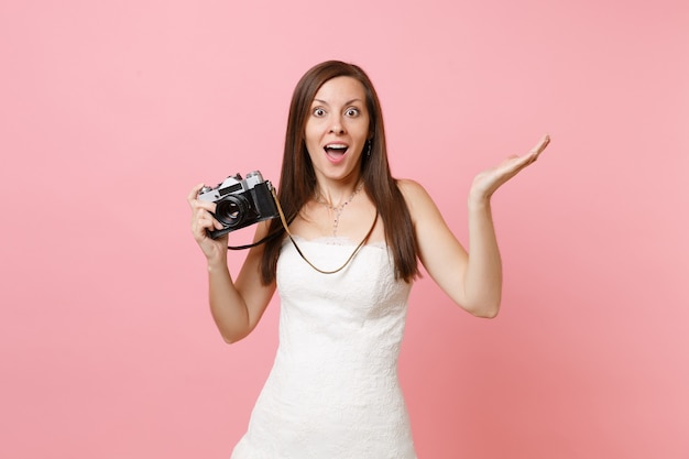 Excited woman in white dress spreading hands holding retro vintage photo camera choosing staff, photographer 