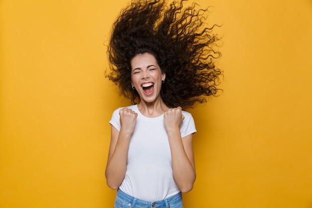 excited woman with shaking hair screaming and rejoicing isolated on yellow
