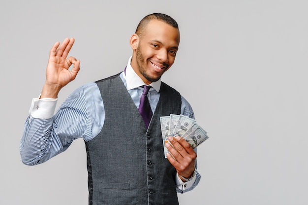  excited young african american man holding cash money and showing OK sign over light grey wall