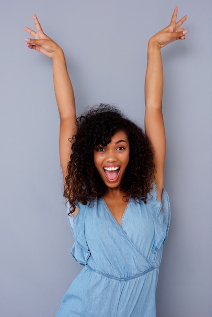 Excited young african american woman smiling with hands raised against gray background