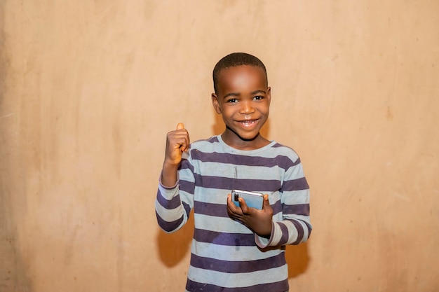 Photo excited young african boy holding mobile phone happy like a winner in casual clothes isolated over yellow studio background