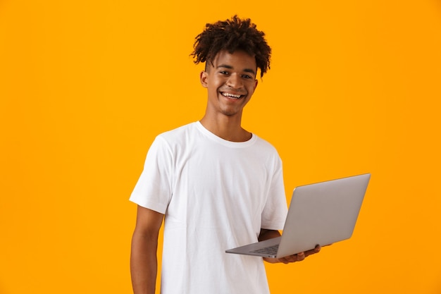노트북 컴퓨터를 사용 하여 노란색 공간 위에 절연 흥분된 젊은 아프리카 남자.