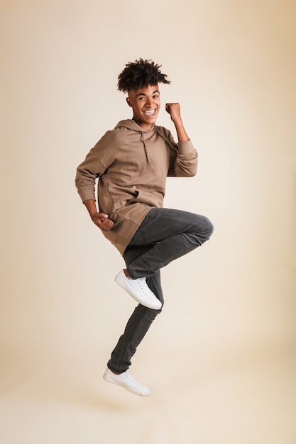 Excited young afro american man dressed in hoodie jumping isolated make winner gesture