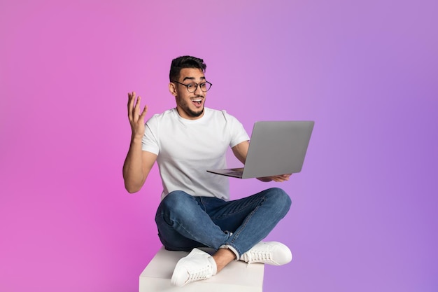 Excited young arab man sitting cross legged with laptop feeling overjoyed over huge online sale in