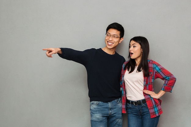 Excited young asian loving couple pointing.