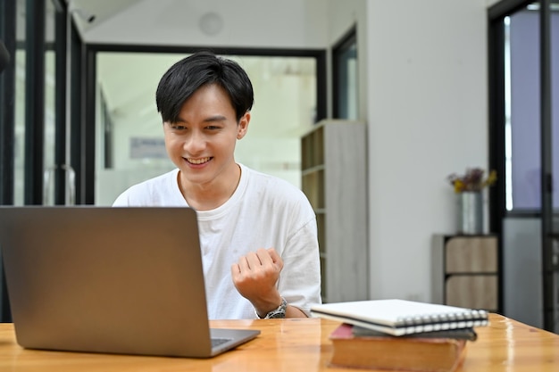 Excited young Asian male looking at his laptop screen getting an unexpected email