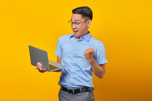 Excited young asian man Asian in glasses using laptop isolated on yellow background businessman and entrepreneur concept