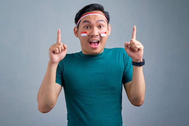 Excited young Asian man in casual tshirt pointing finger up having an idea or found solution isolated on grey background indonesian independence day celebration concept