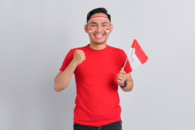 Excited young Asian man celebrating Indonesian independence day holding the Indonesian flag isolated on white background