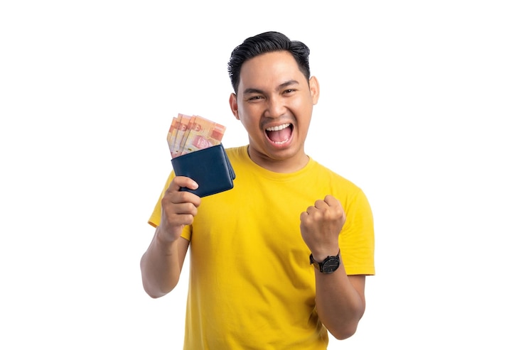 ワクワクした若いアジア人男性が財布に現金を持ち白い背景に隔離された拳を上げています利益と富の概念
