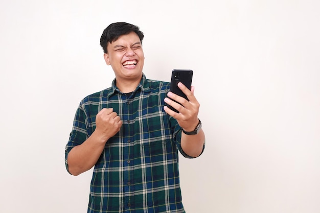 Возбужденный молодой азиатский мужчина с кулаком в руке, держащий сотовый телефон.