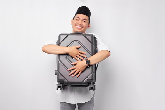 Excited young Asian Muslim man hugging a suitcase and ready to go for the holiday eid Mubarak isolated on white background Ramadan and eid Mubarak concept