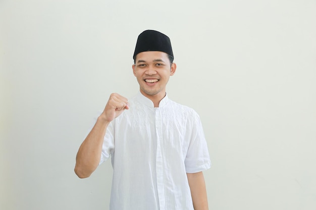 Excited young Asian Muslim man raising fists and celebrating victory on Ramadan