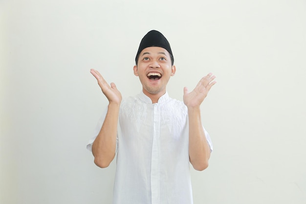 Excited young Asian Muslim man raising fists and celebrating victory on Ramadan