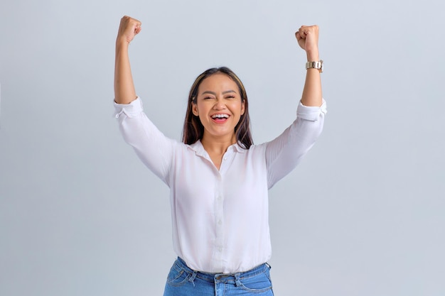 Excited young Asian woman celebrating victory or success with raised fists up isolated over white background