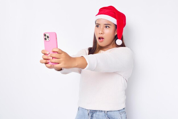 Excited young Asian woman in a Christmas hat looking at smartphone getting great news isolated over white background celebration Christmas holiday and New Year concept