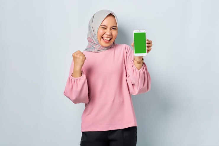 Excited young Asian woman in pink shirt showing mobile phone blank screen recommending App isolated over white background