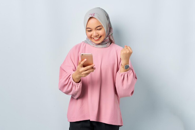 Excited young Asian woman in pink shirt using mobile phone received good news isolated over white background