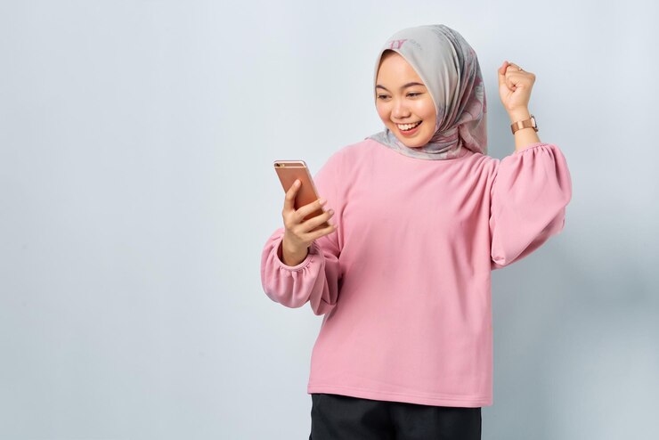 Excited young Asian woman in pink shirt using mobile phone received good news isolated over white background